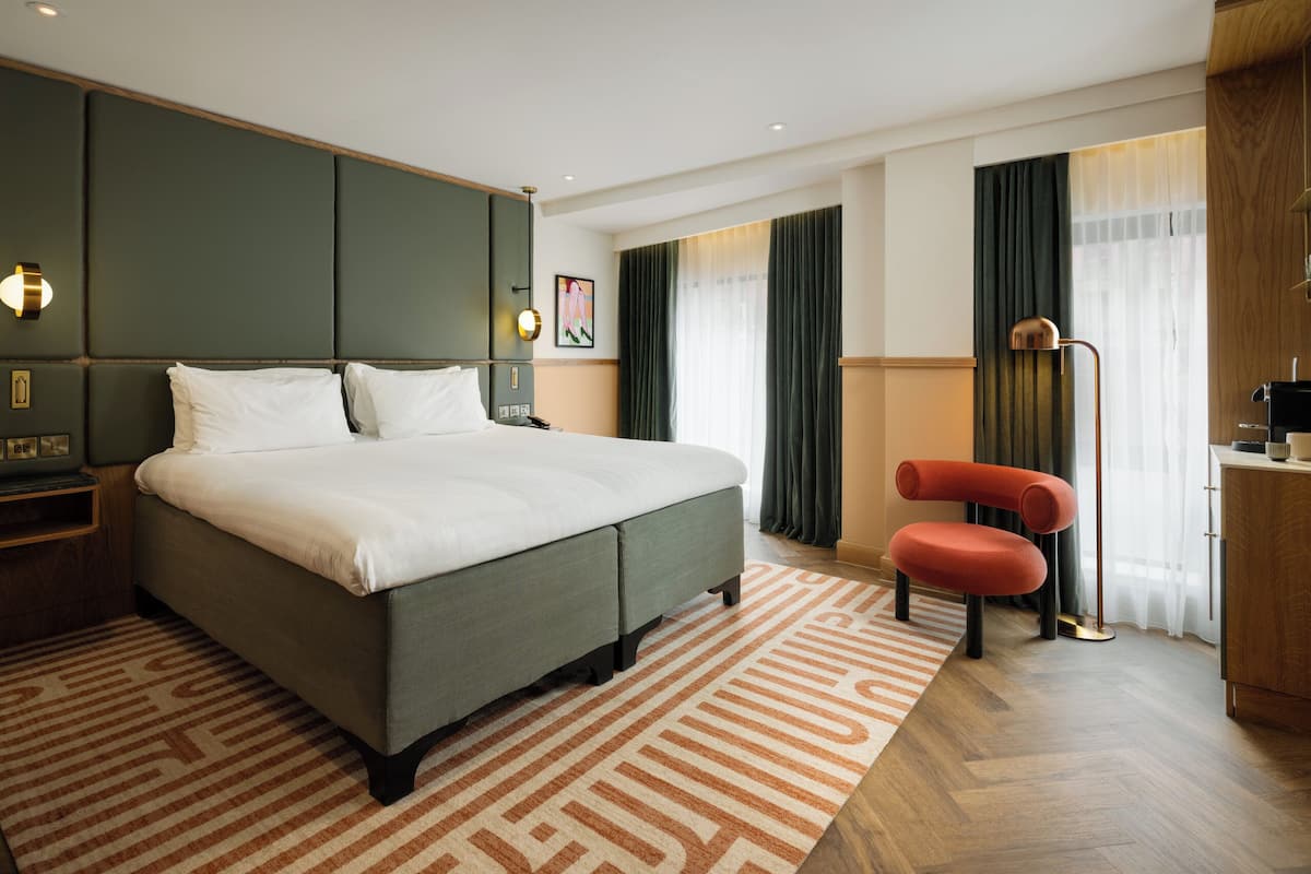 A modern hotel room with a large bed, a desk, a chair, and a desk lamp.