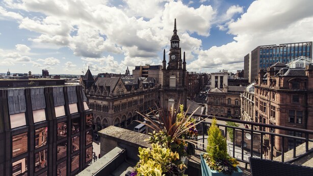 A historic building with a clock tower, surrounded by modern architecture and a clear sky. - Carlton George Hotel (Glasgow)