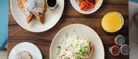 A breakfast setting with various dishes including toast, croissants, eggs, and a glass of orange juice.