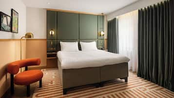 Una moderna camera d'albergo con un letto grande, un'area salotto con una poltrona, un tavolino e una lampada a parete.