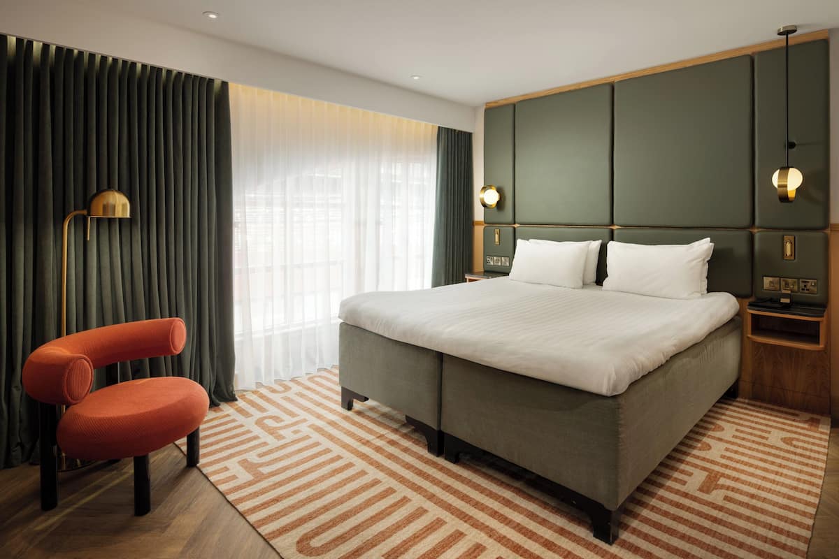 A hotel room with a large bed, a chair, a desk, and a lamp.