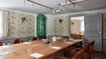 Un salón de conferencias con una larga mesa de madera, sillas, un proyector y papel tapiz floral.