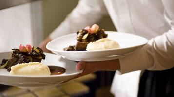 A person holding two plates of food, one with a dark dish and the other with a lighter dish, possibly in a restaurant or dining setting.