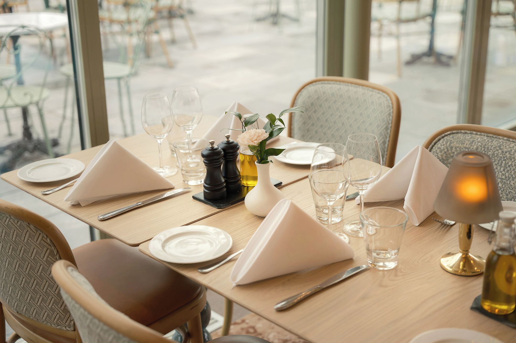 A dining table set with white napkins, plates, cutlery, and glasses, with a salt and pepper set, a flower vase, and a lamp.