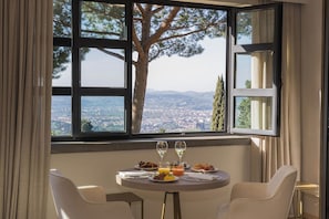 Una mesa de comedor con vistas panorámicas a través de amplios ventanales, dos copas de vino blanco y una comida.