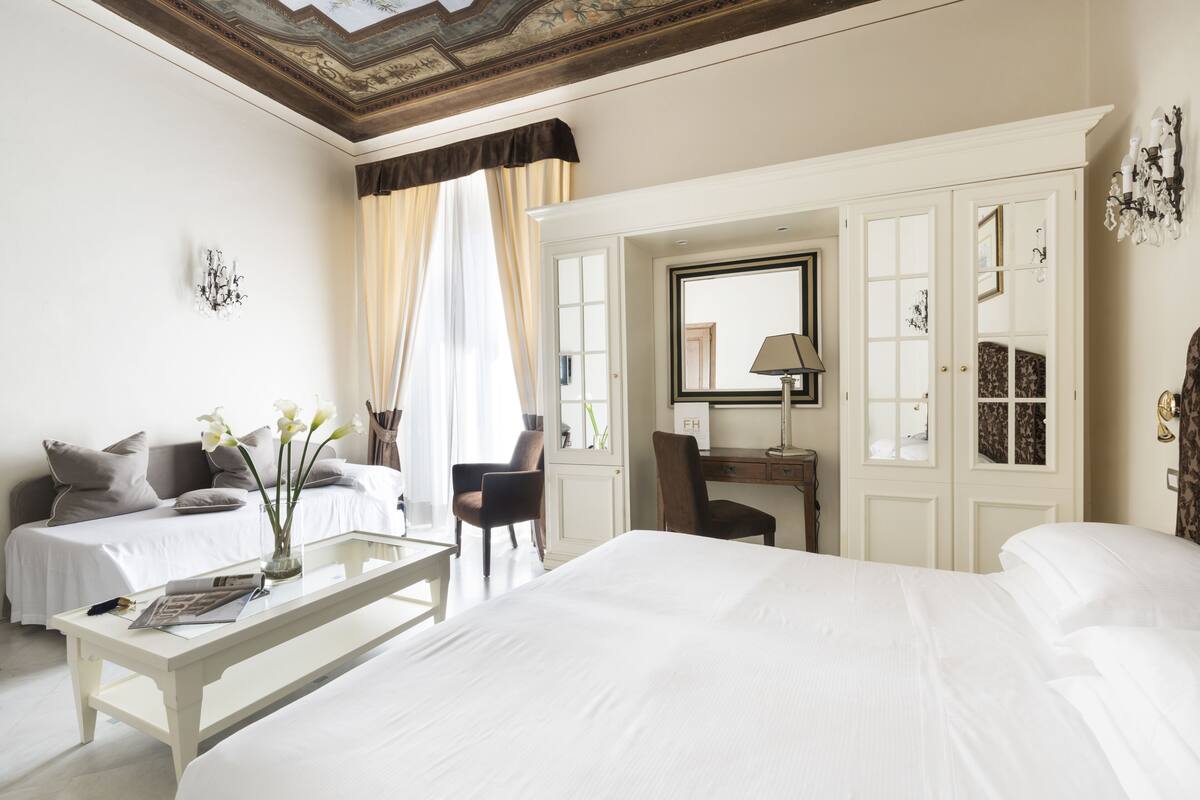 Habitación de hotel con una cama grande, una zona de estar con mesa y sillas, un escritorio con lámpara y un armario.