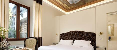 A hotel room with a large bed, a desk with a vase, and a ceiling with detailed artwork.