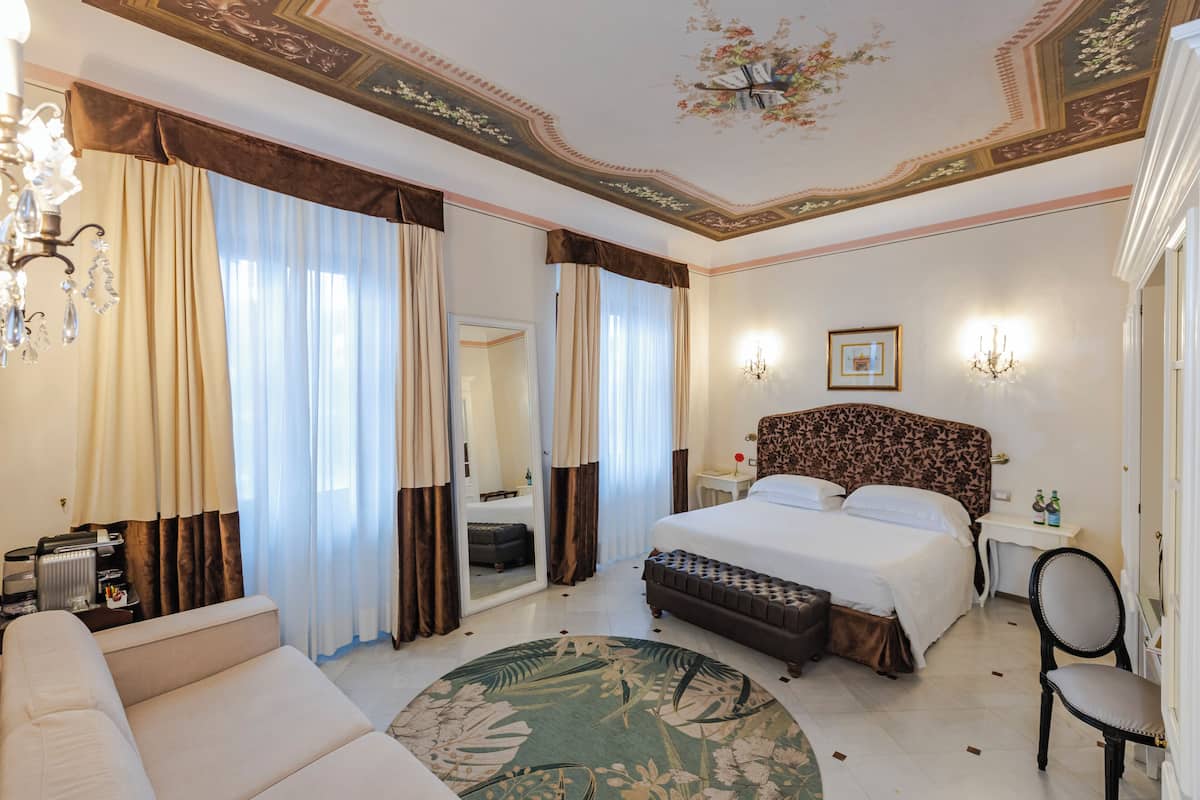 Una habitación de hotel con una cama grande, una zona de estar, un espejo y un candelabro.