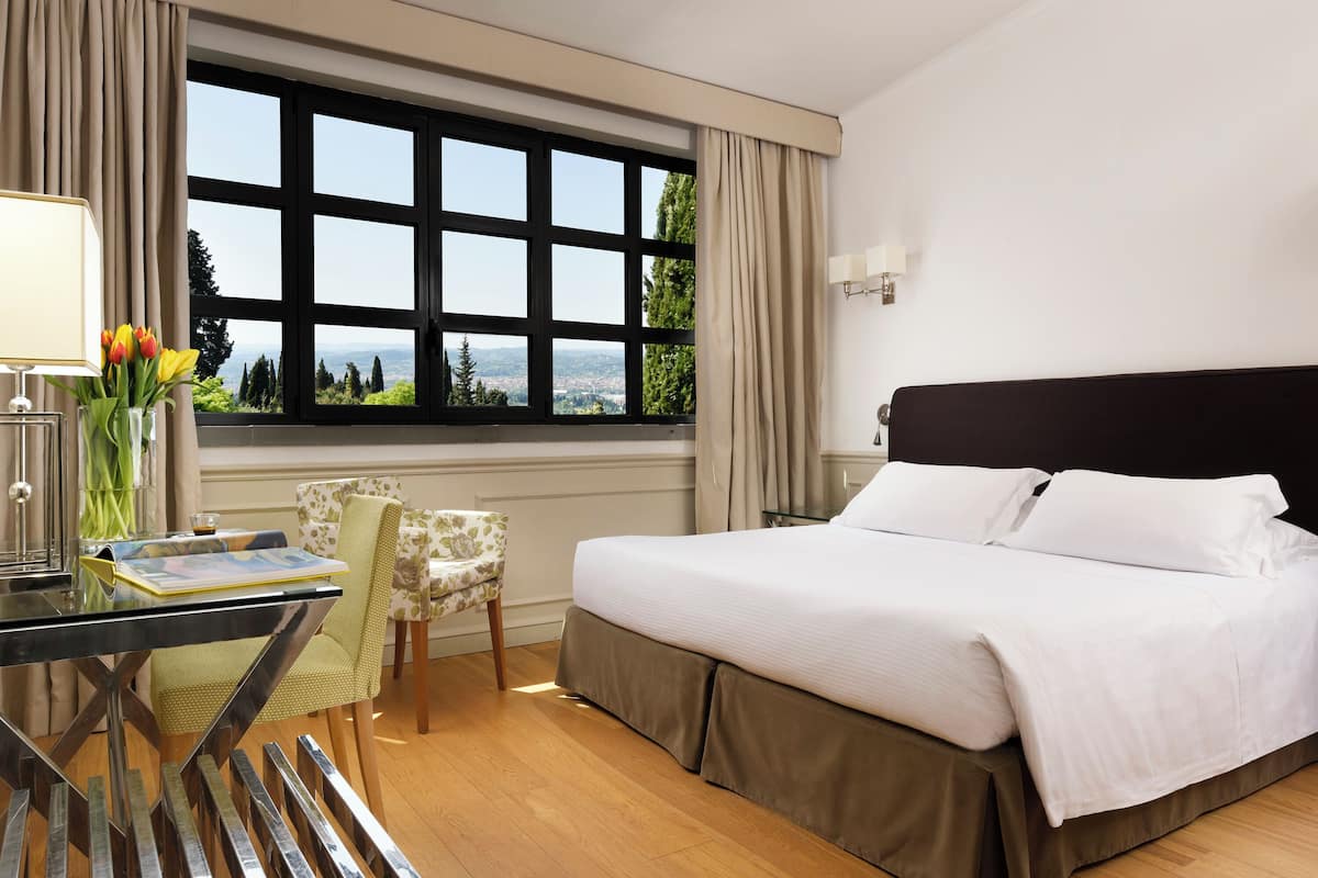 Habitación de hotel con una ventana grande, una cama, un escritorio con lámpara y una silla.