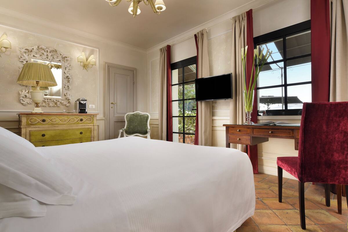 Habitación de hotel con una cama grande, un escritorio con silla, televisor y una ventana con cortinas.
