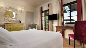 A hotel room with a large bed, a desk with a chair, a television, and a window with curtains.