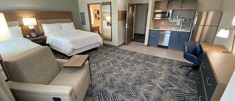 A hotel room with a bed, a sofa, a desk, a kitchenette, and a bathroom.