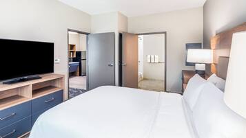Habitación de hotel con cama, televisor, armario y baño visible a través de una puerta abierta.