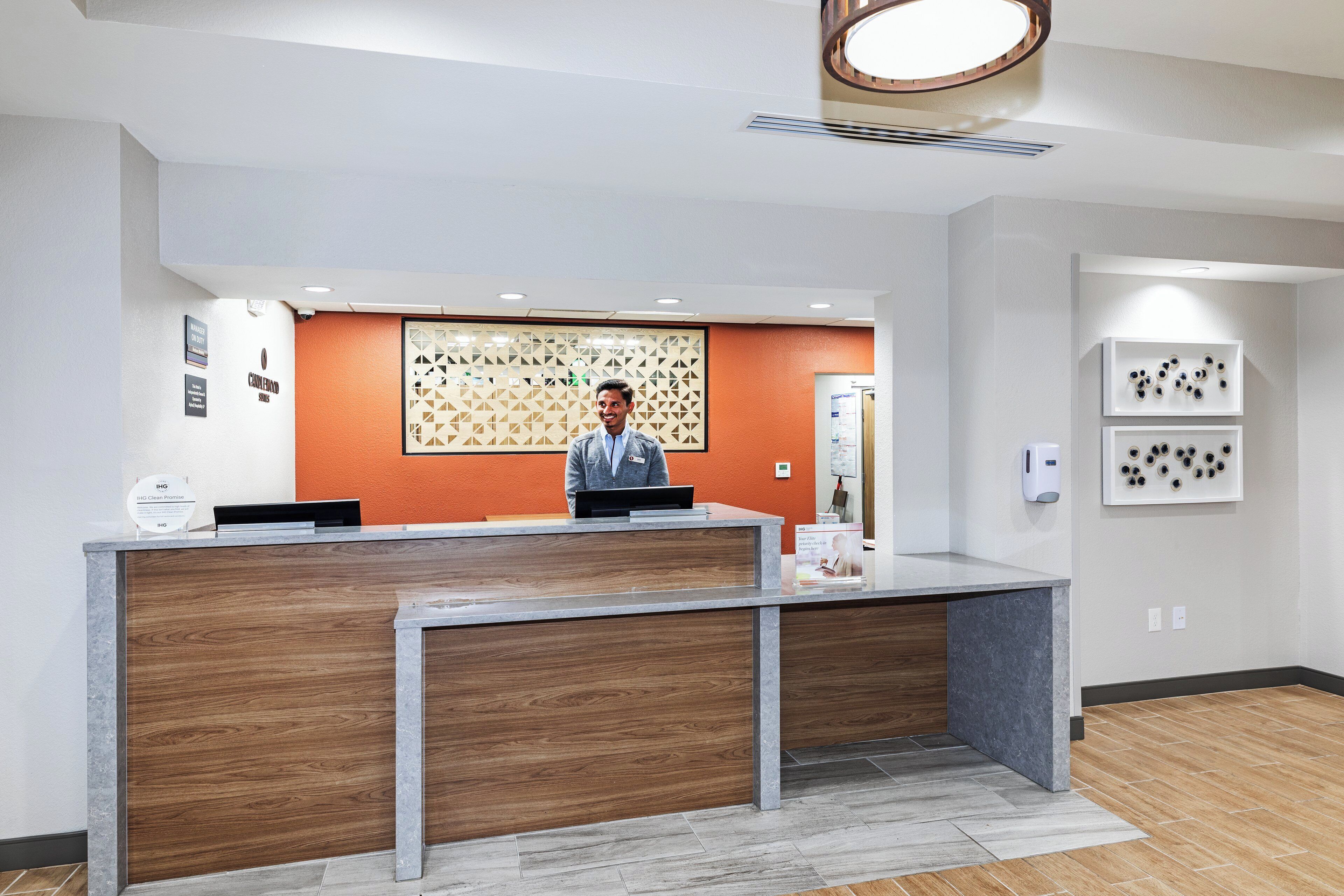 A reception desk with a wooden panel design, a man standing behind it, and a wall with framed pictures.