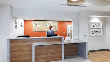 A reception desk with a wooden panel design, a man standing behind it, and a wall with framed pictures.