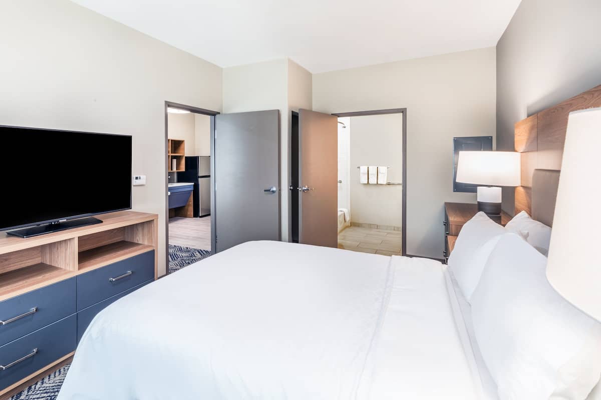 Une chambre d’hôtel équipée d’un lit, d’une télévision, d’une armoire, d’une salle de bain et d’une table de chevet avec une lampe.