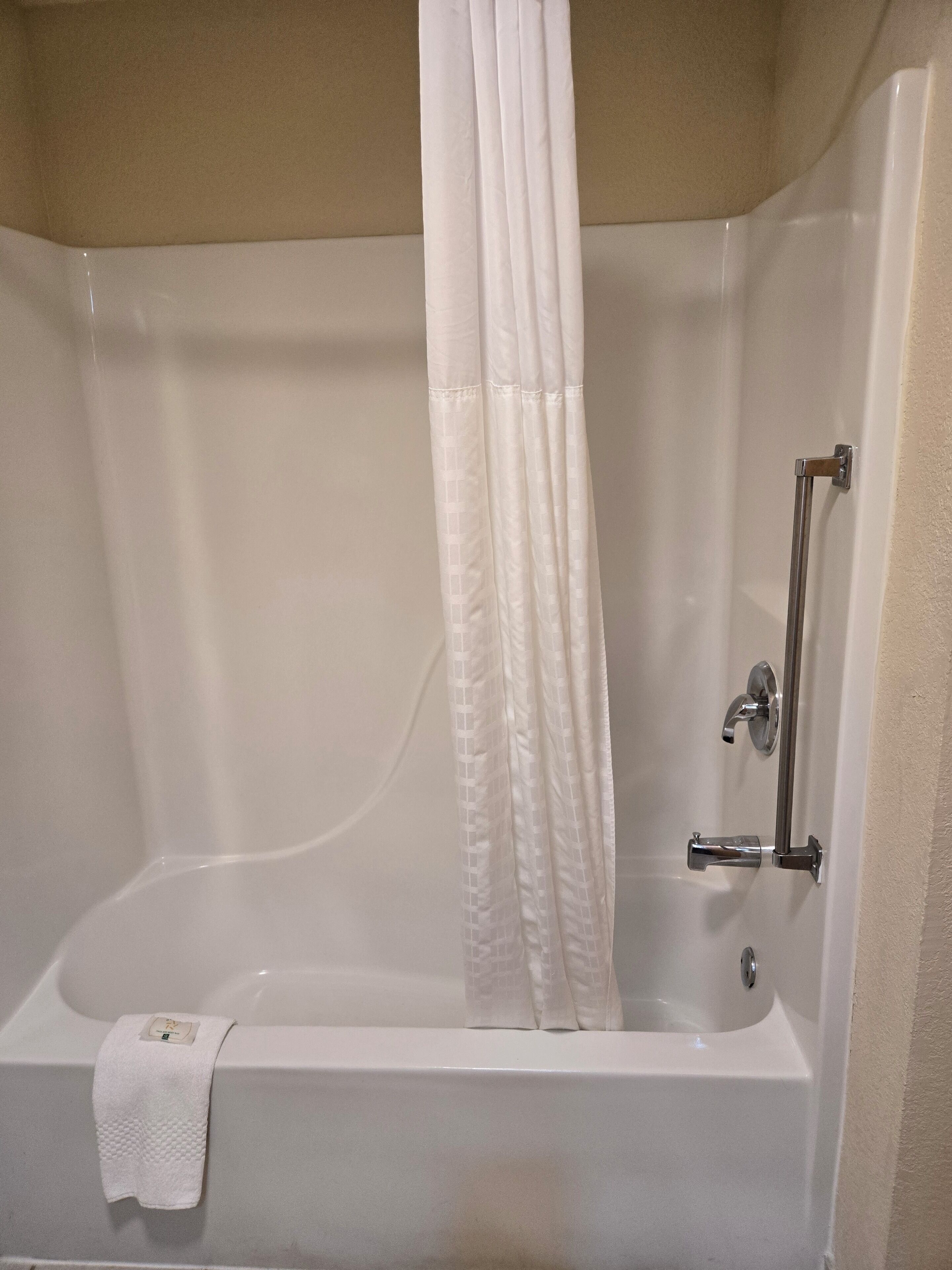 Una bañera con cortina de ducha, una toalla y un grifo de cromo.