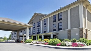 A multi-story hotel with a covered parking area, a landscaped garden with colorful flowers, and a clear blue sky. - Quality Inn & Suites Boone - University Area (Boone)