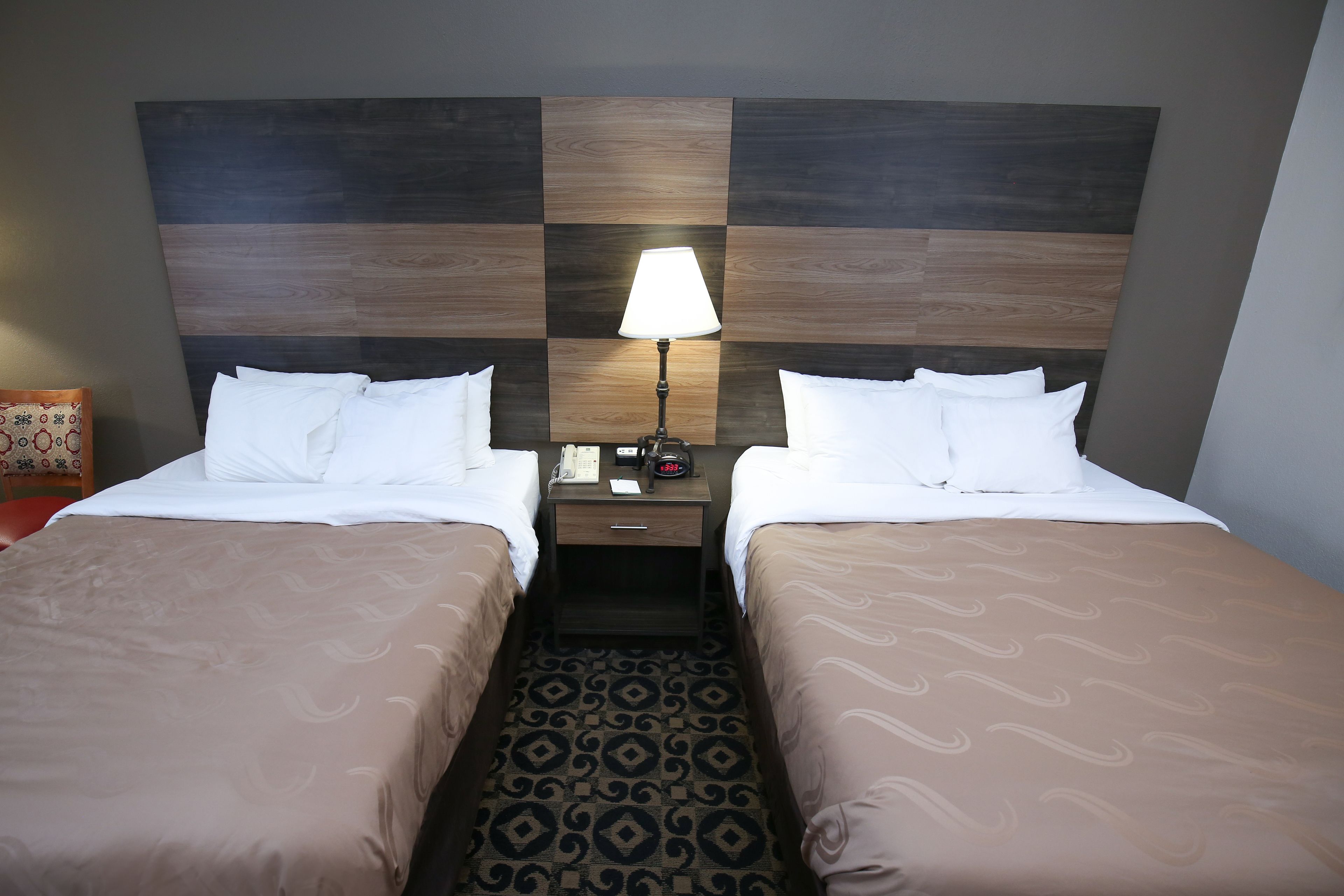 Une chambre d’hôtel avec deux lits, une table de chevet avec une lampe et une moquette à motifs.