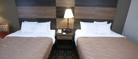 A hotel room with two beds, a nightstand with a lamp, and a patterned carpet.