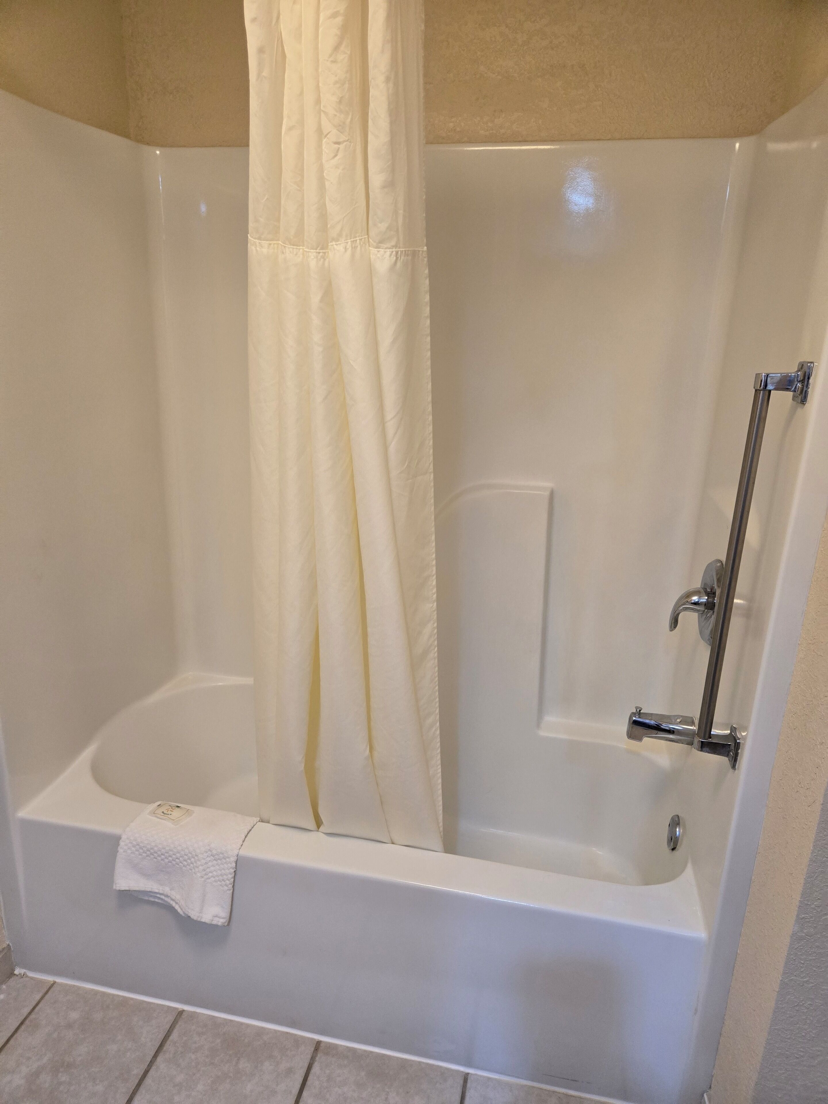 A corner bathtub with a shower curtain, a handheld showerhead, and a towel rack.