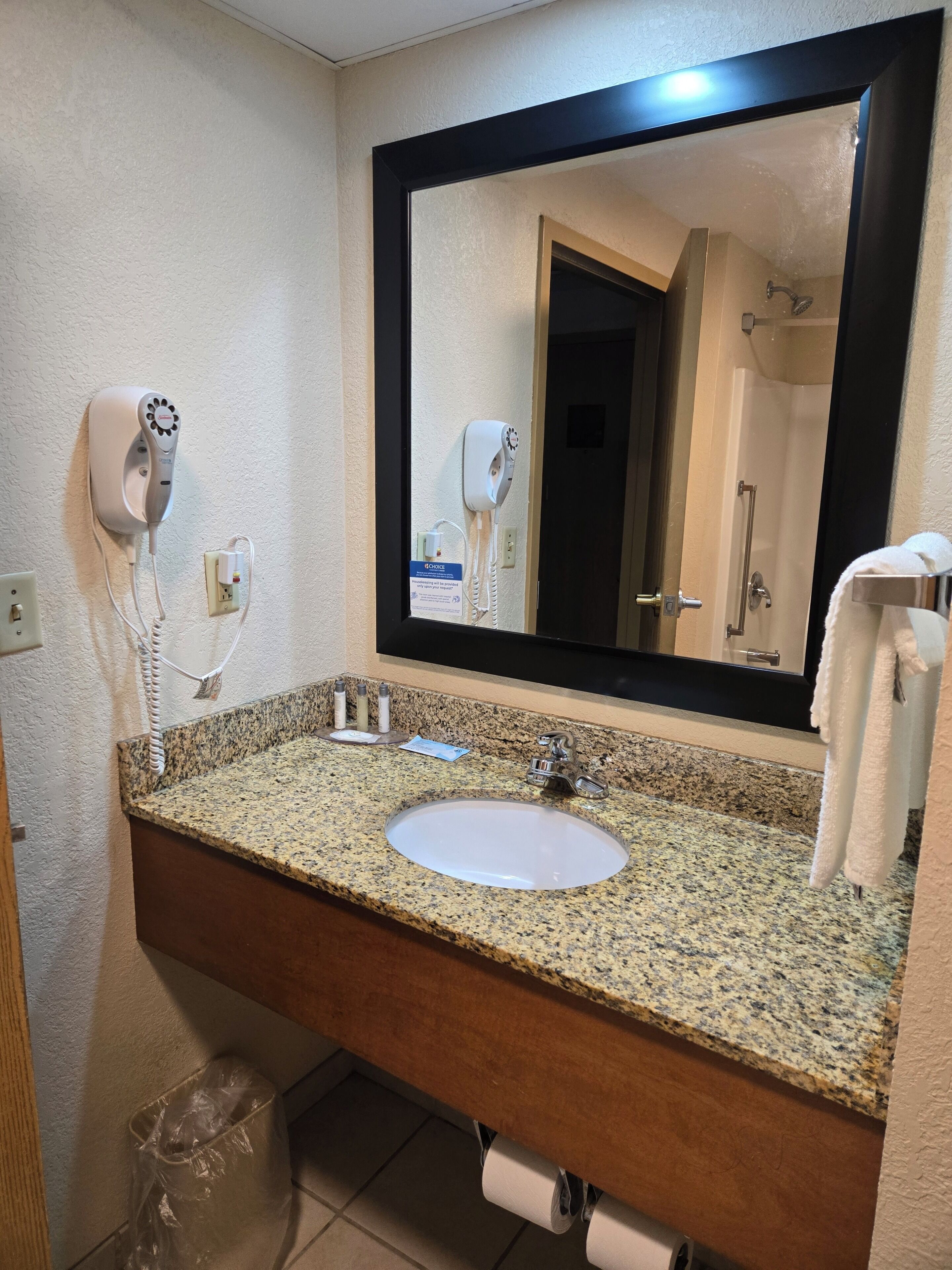 A bathroom with a granite countertop, a sink, a mirror, a hairdryer, and a towel rack.