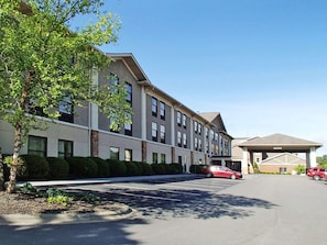 A multi-story hotel with a parking lot, a covered entrance, and a row of trees along the building facade.