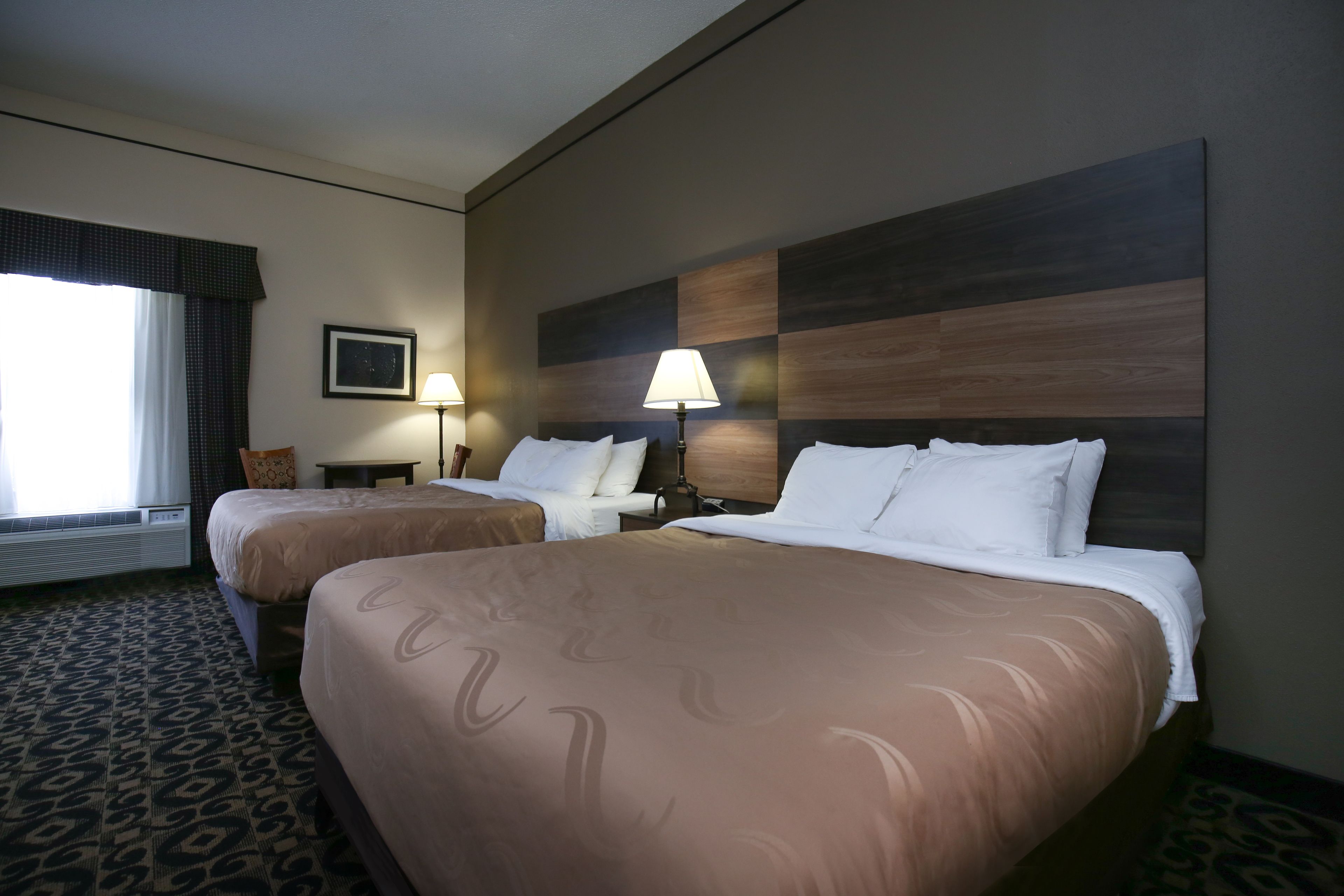 Habitación de hotel con dos camas, un ventanal con cortinas, una lámpara de pared y un cuadro en la pared.