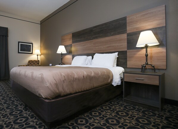 A hotel room with a large bed, two bedside lamps, a nightstand, and a patterned carpet.