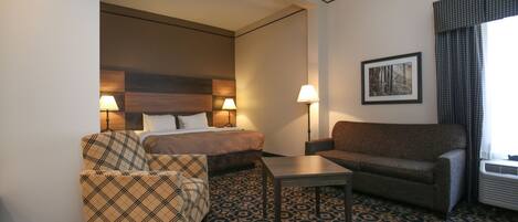 Una habitación de hotel con una cama, dos sillas, una mesita y un cuadro en la pared.
