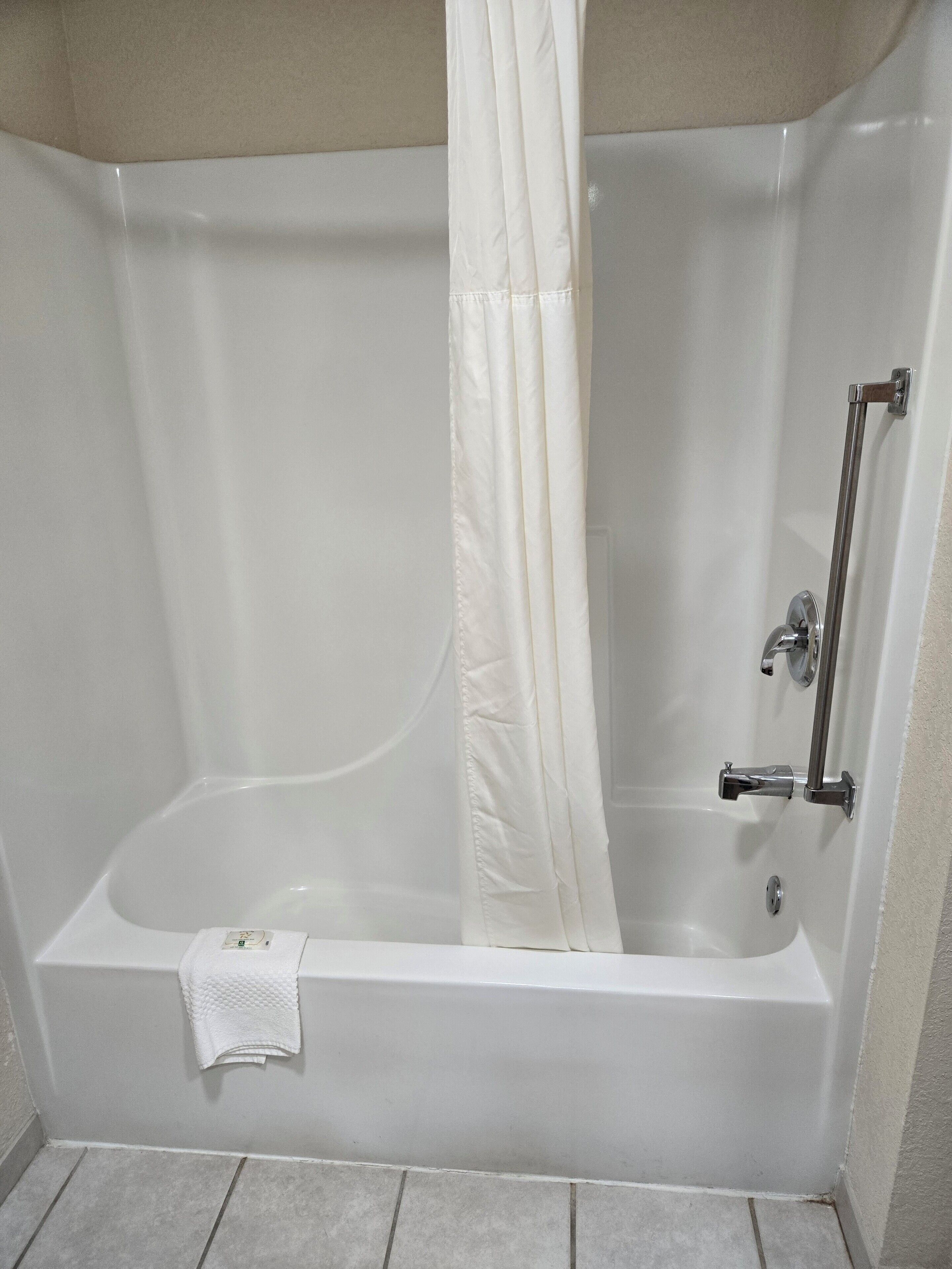 A bathtub with a shower curtain, a handheld showerhead, and a towel on the floor.