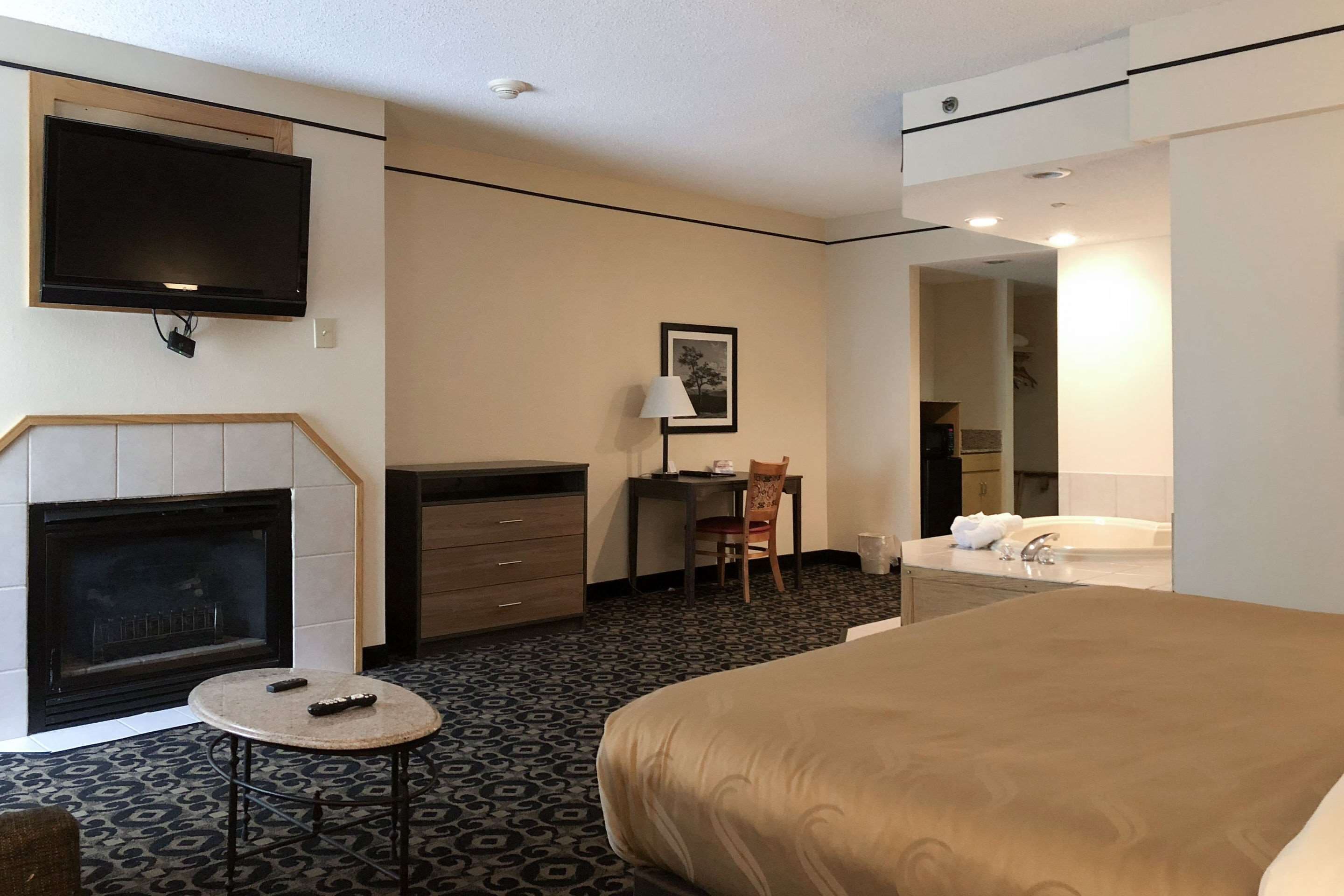 Hotelkamer met een bed, een open haard, een bureau met stoel, een televisie, en een badkamer met badkuip en wastafel.