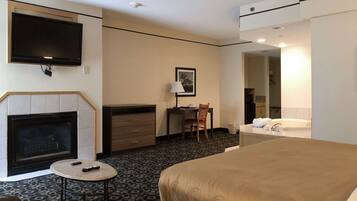 Hotelkamer met een bed, een open haard, een bureau met stoel, een televisie, en een badkamer met badkuip en wastafel.