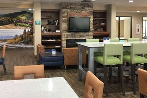 A restaurant with a stone wall, a flat-screen TV, and green cushioned chairs.