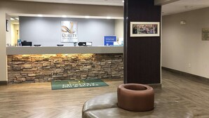 A reception area with a stone wall, a reception desk, and a green mat with the hotel name. - Quality Inn & Suites Boone - University Area (Boone)