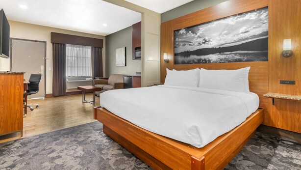 A modern hotel room with a large bed, a desk, a chair, and a view of the outdoors. - Best Western Plus Yukon (Yukon)