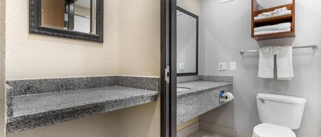 A bathroom with a granite countertop, a mirror, a toilet, and a towel rack.