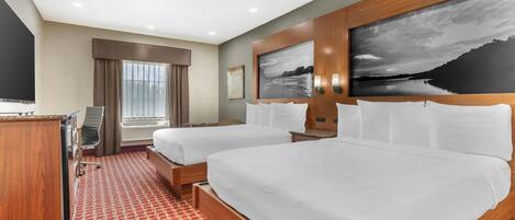 Habitación de hotel con dos camas, un escritorio, un televisor y un ventanal con cortinas.