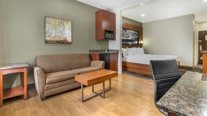 A hotel room with a bed, a sofa, a small table, a chair, a microwave, and a painting on the wall. - Best Western Plus Yukon (Yukon)