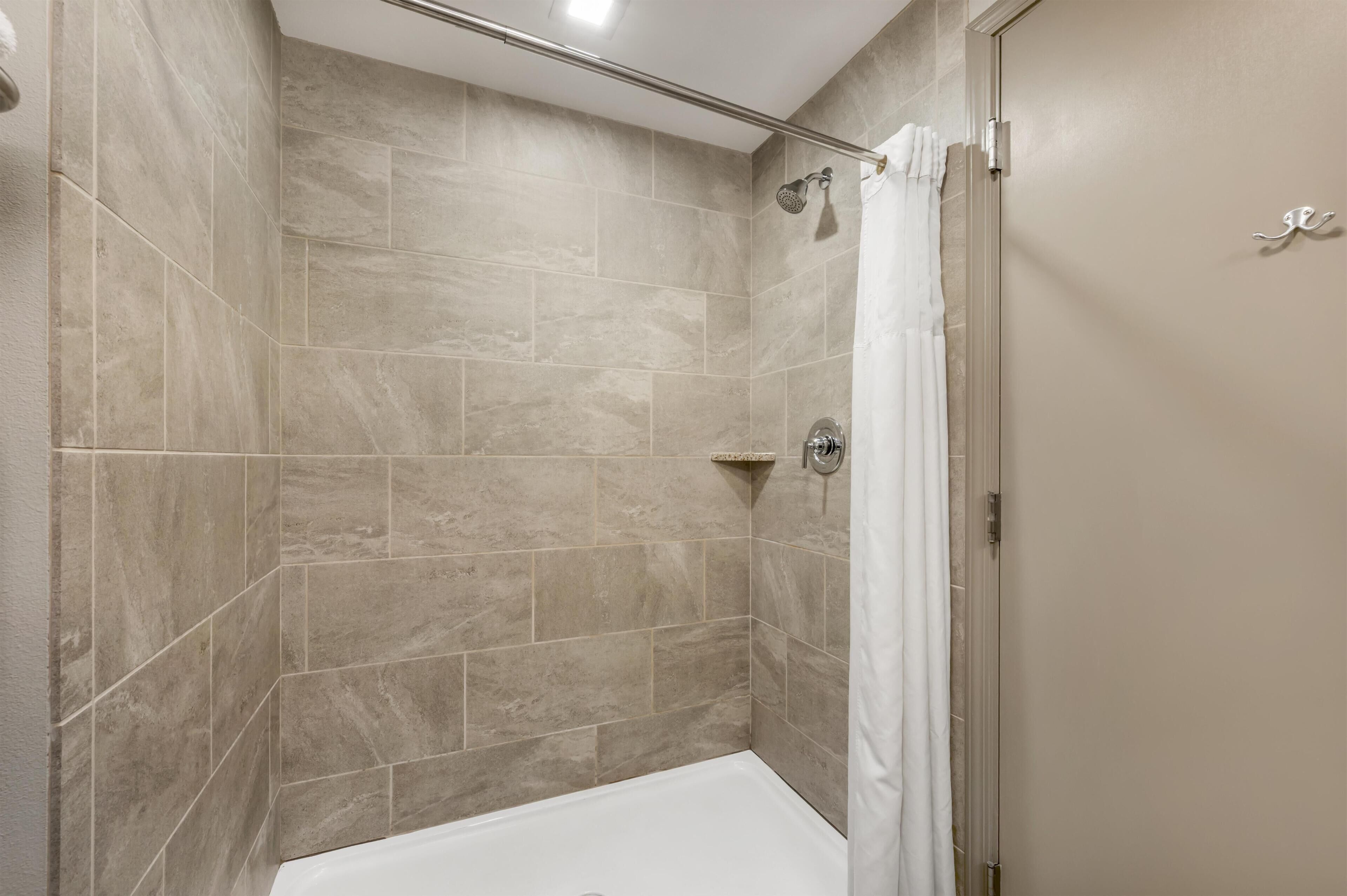 A shower with beige tiles, a white bathtub, and a shower curtain.