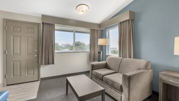Ein Hotelzimmer mit einer Couch, einem kleinen Tisch, einer Lampe, einer Tür und einem Fenster mit Vorhängen.
