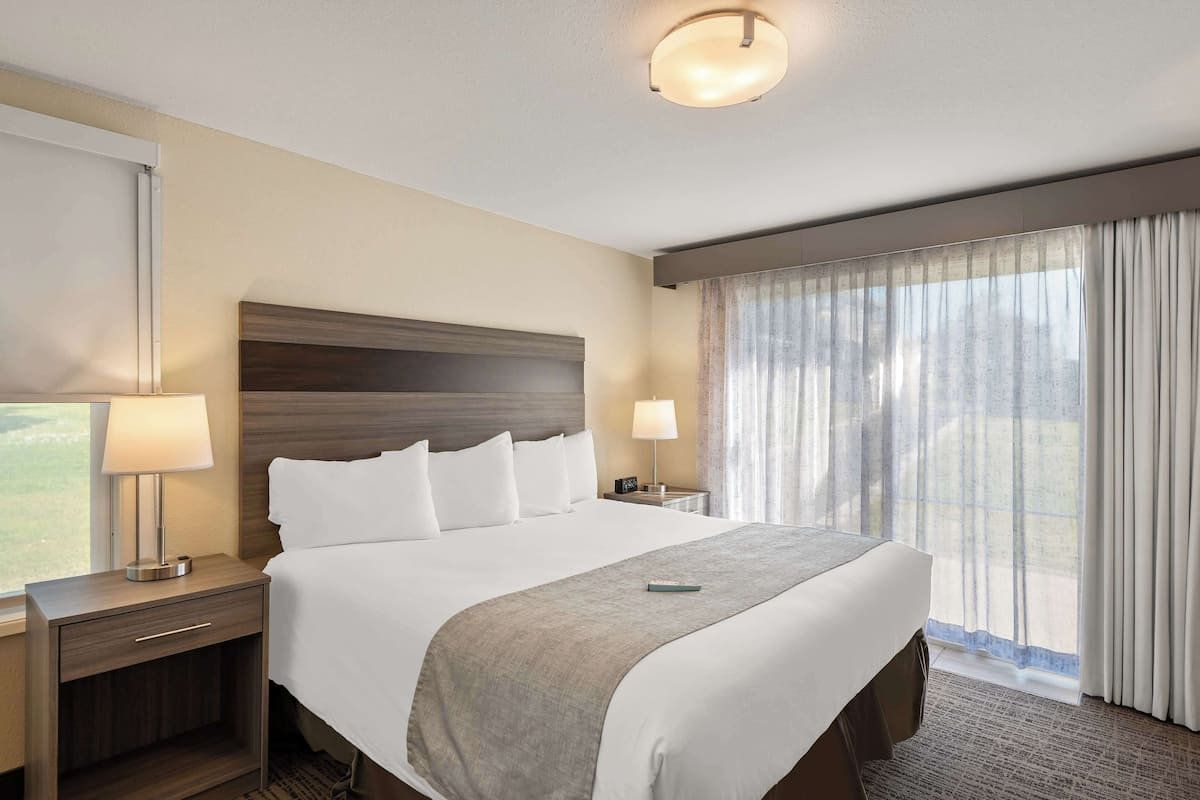 Una habitación de hotel con una cama grande, dos mesitas de noche, una lámpara, un control remoto y una ventana con cortinas.