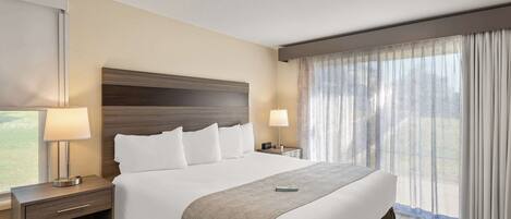 Una habitación de hotel con una cama grande, dos mesitas de noche, una lámpara, un control remoto y una ventana con cortinas.