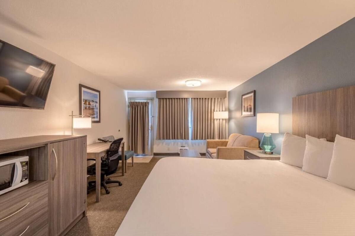 Habitación de hotel con una cama grande, un escritorio con una silla, un televisor y una ventana con cortinas.