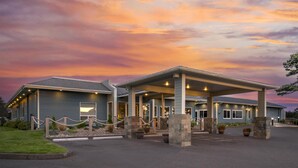 Un hôtel doté d’une entrée abritée, d’un espace extérieur aménagé pour s’asseoir et d’une allée bordée de verdure.