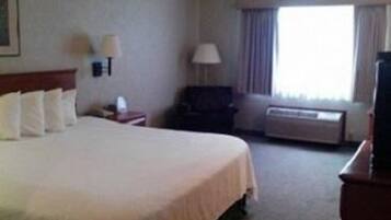 A hotel room with a large bed, a desk with a lamp, a chair, a TV, and a window with curtains.