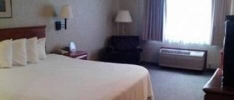 A hotel room with a large bed, a desk with a lamp, a chair, a TV, and a window with curtains.
