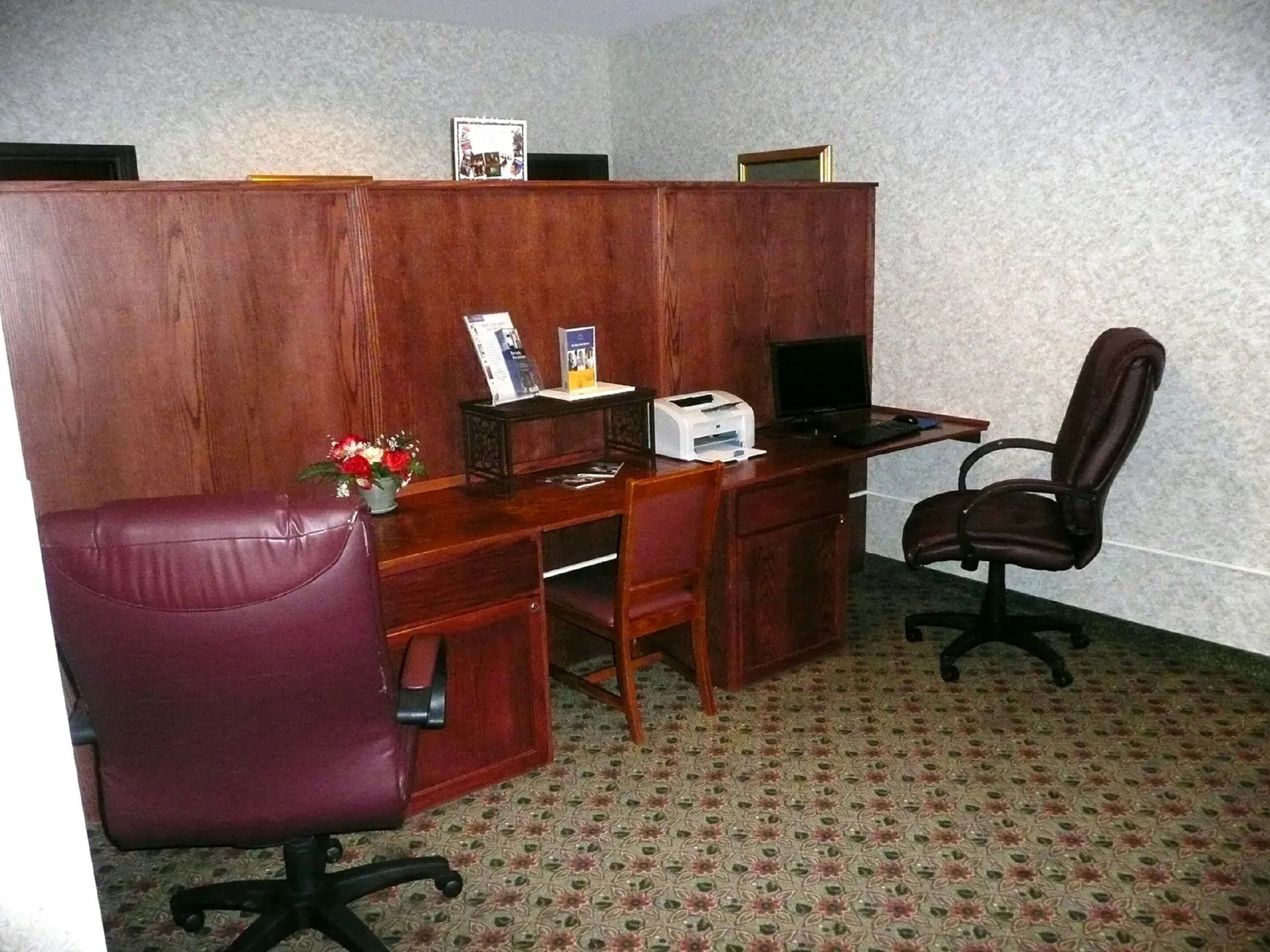 A private office with a wooden desk, two chairs, a printer, and a small plant.