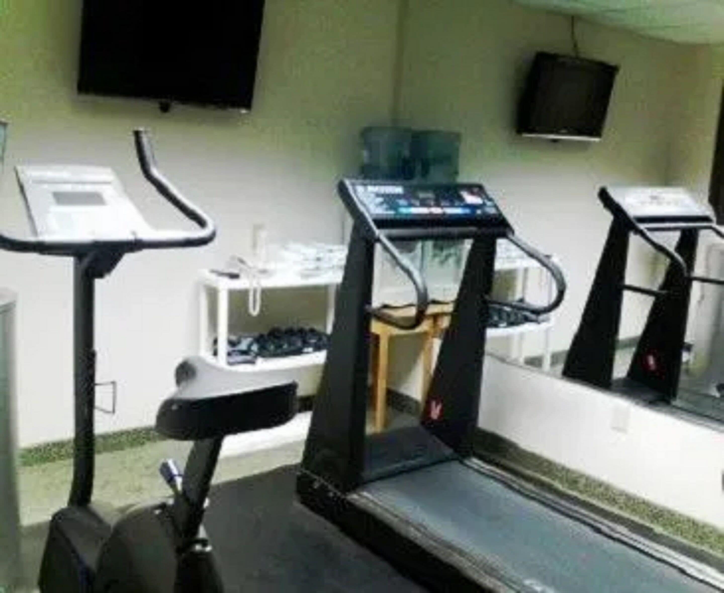 Una cinta de correr en una habitación con un televisor montado en la pared y un dispensador de agua.