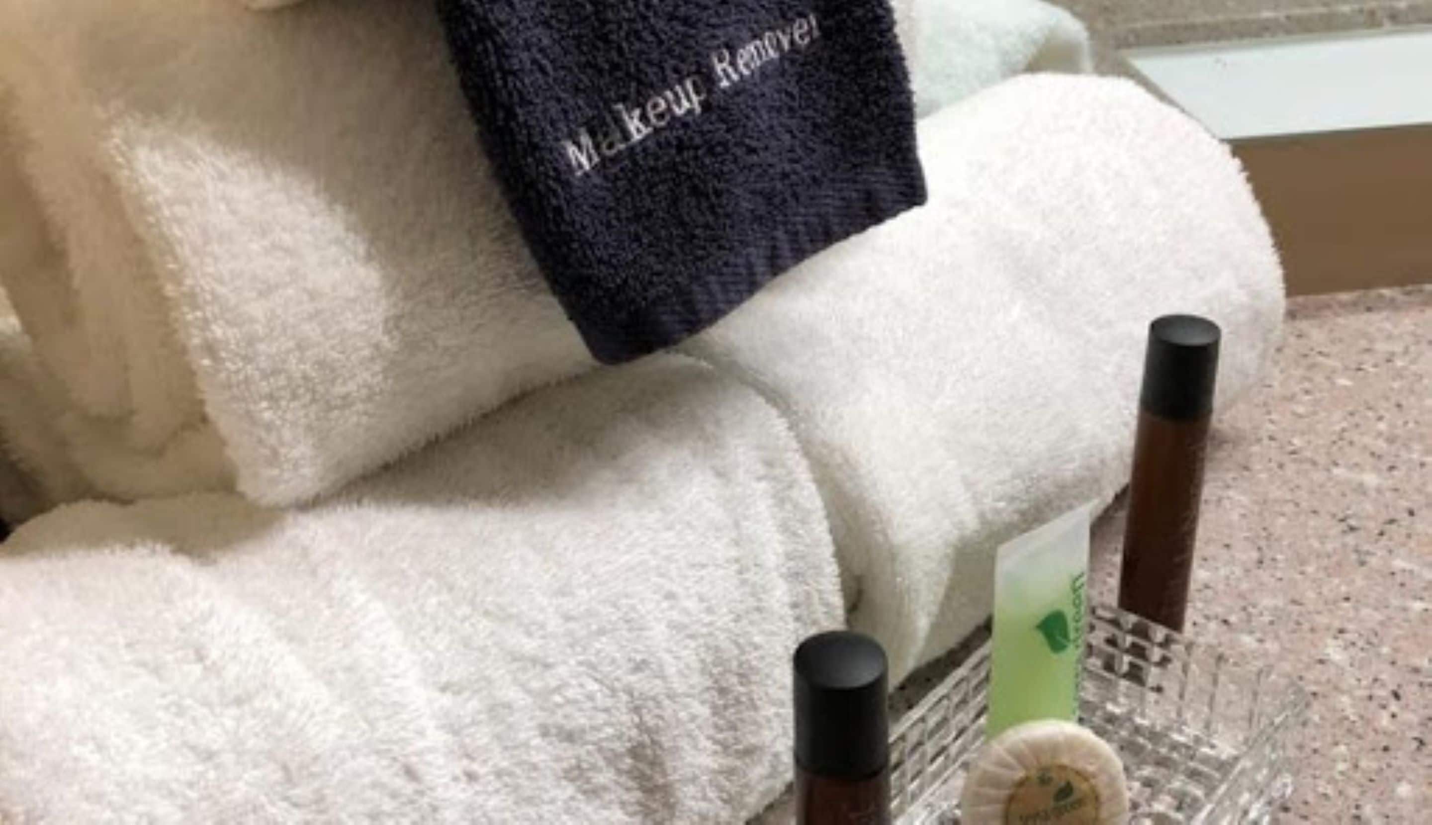 A white towel with a black label that reads "Makeup Remover" and two small bottles on a tray.